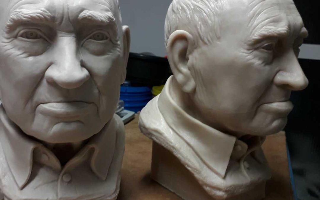 Two clay busts of an elderly man, displayed side by side on a wooden surface. The bust on the left has "Al Tio Miguel" inscribed on its base.